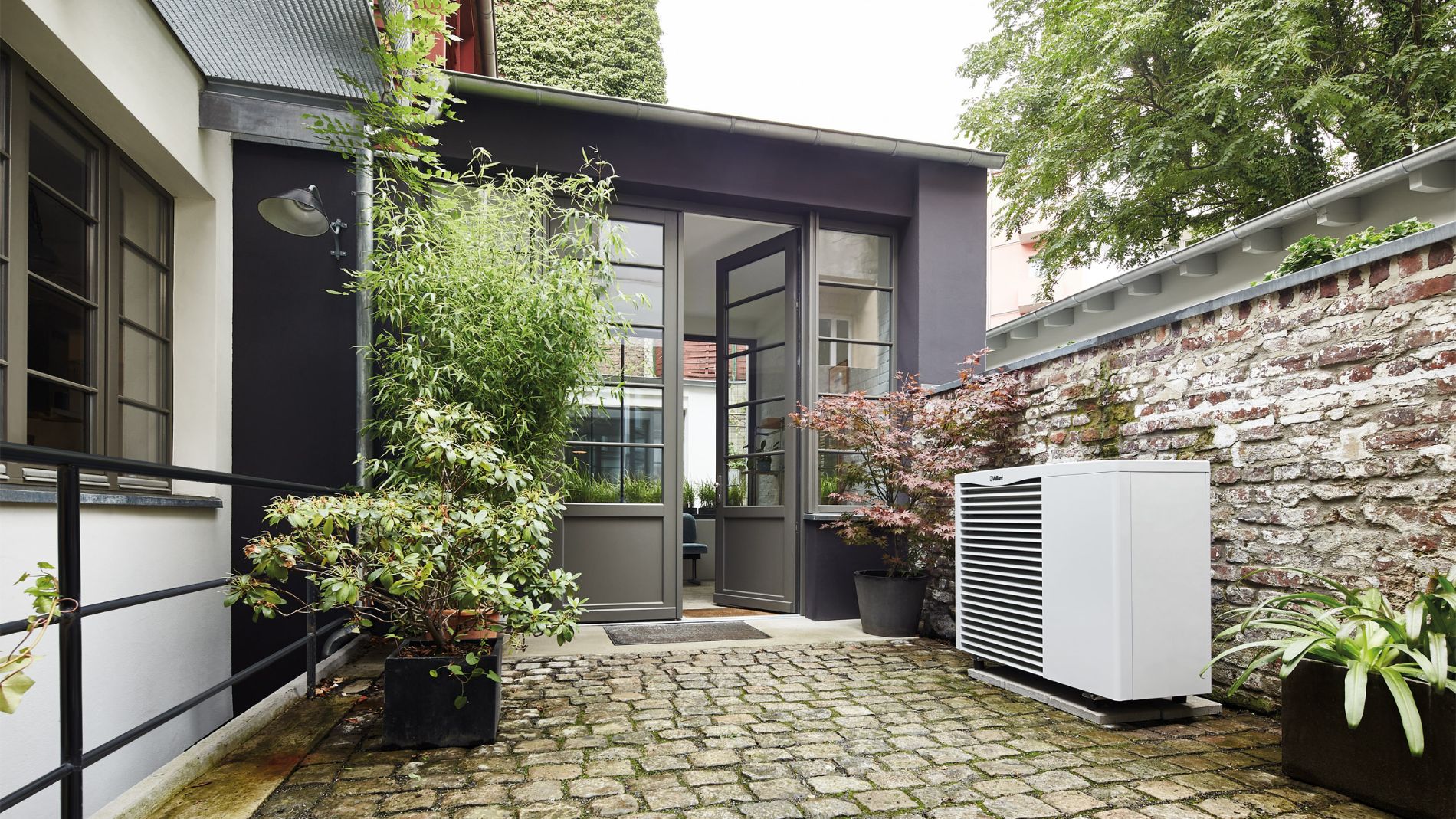 Modern heat pump in a green courtyard in front of a residential building, illustrating energy-efficient heating technology in an urban setting.