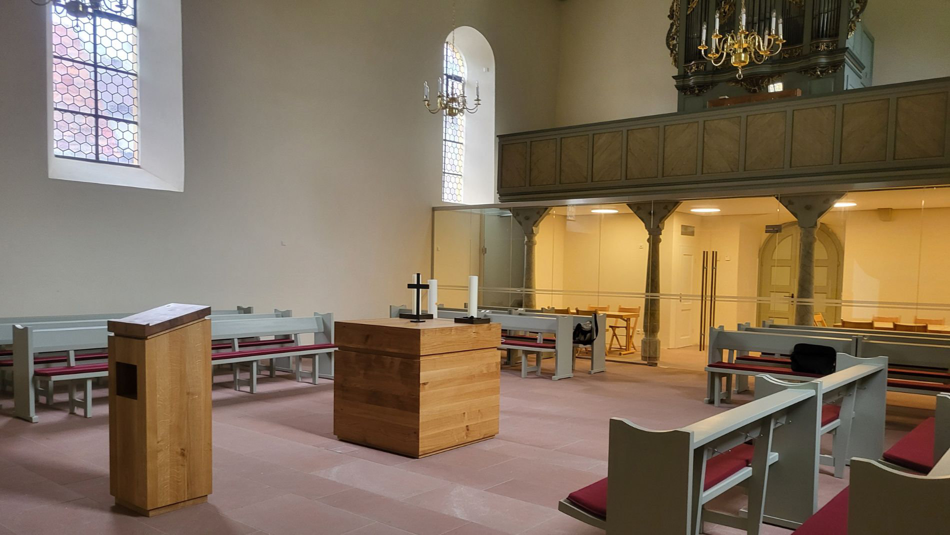 Innenansicht einer sanierten historischen Kirche mit neu gestaltetem Altarbereich, Holzmöbeln und Glaswand zur Empore.