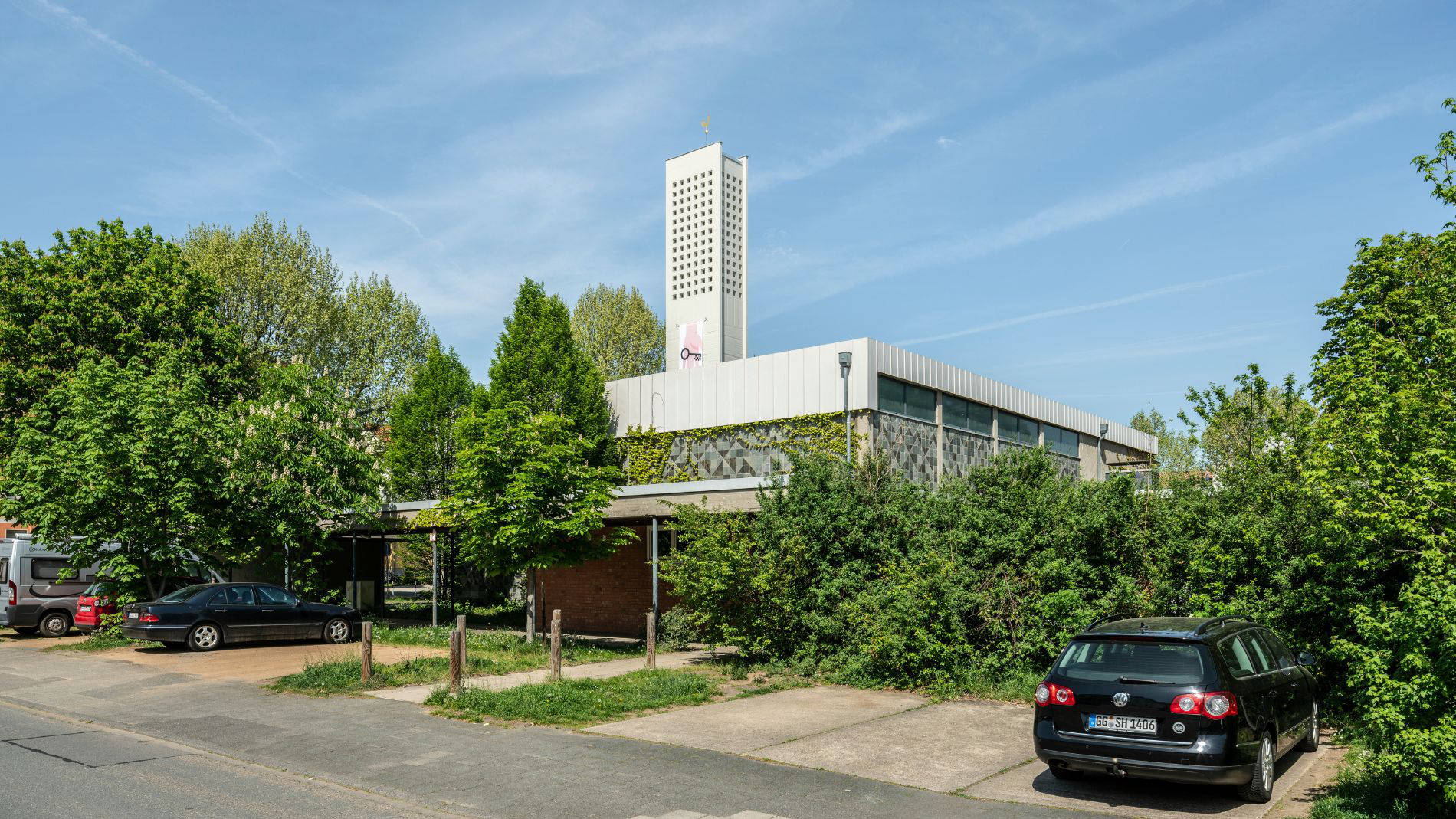 Außenansicht der Kirche Haßloch Nord vor dem Umbau mit Turm, Flachdach und begrünter Fassade.