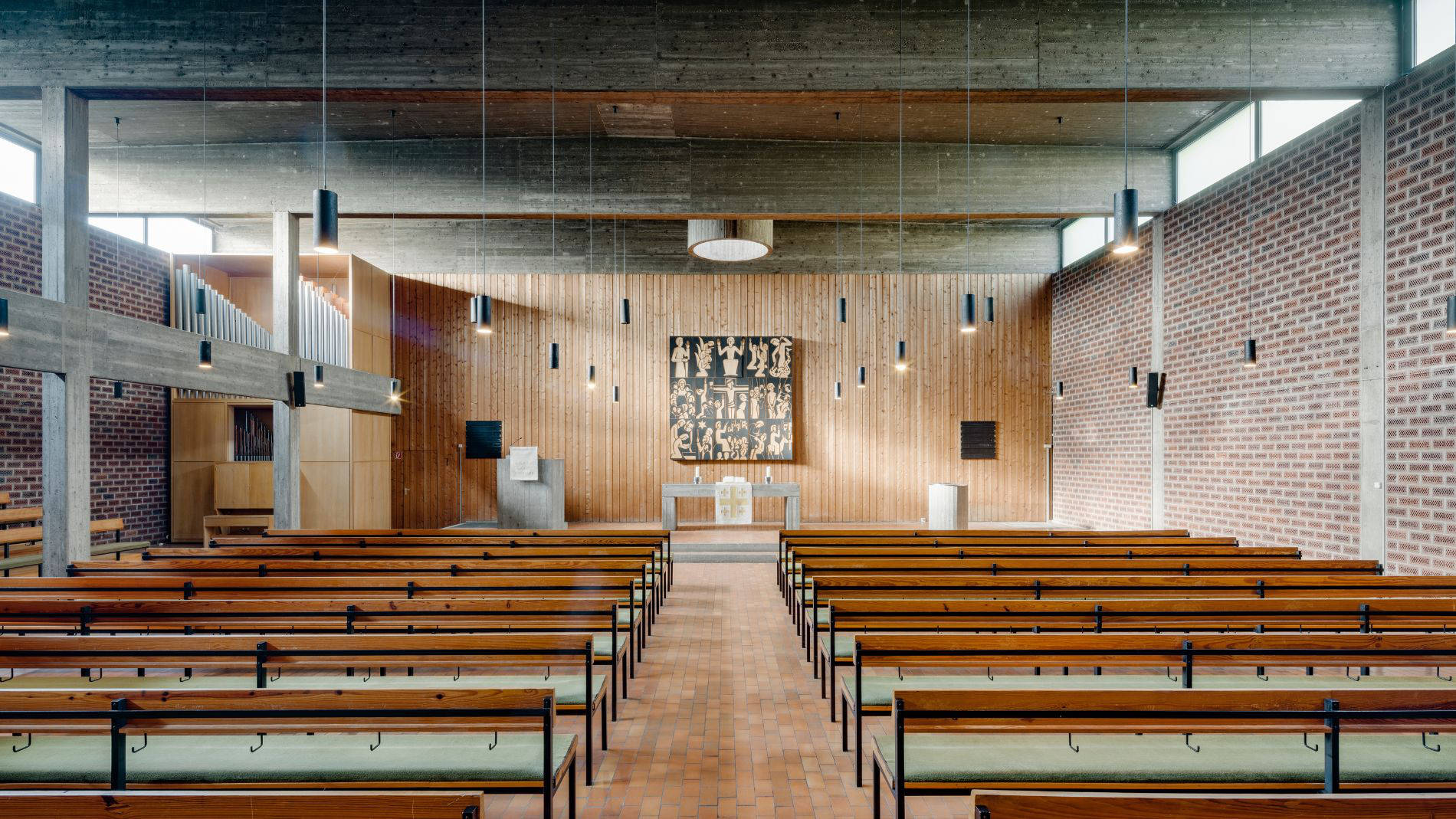 Innenraum der Kirche Haßloch Nord vor dem Umbau, mit Holzbänken, Orgel und Wandverkleidung aus Holz im modern-brutalistischen Stil.