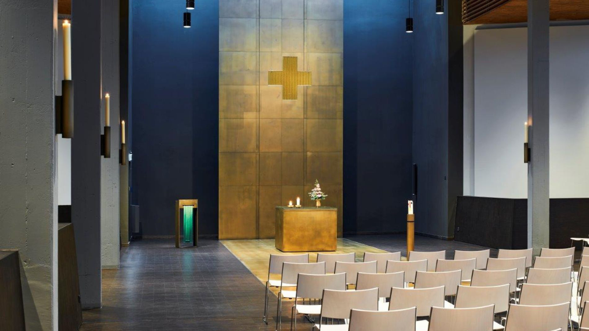 Neugestalteter Kirchenraum der Kirche Rüsselsheim mit bronzefarbenem Altar, Wandkreuz und moderner Beleuchtung.