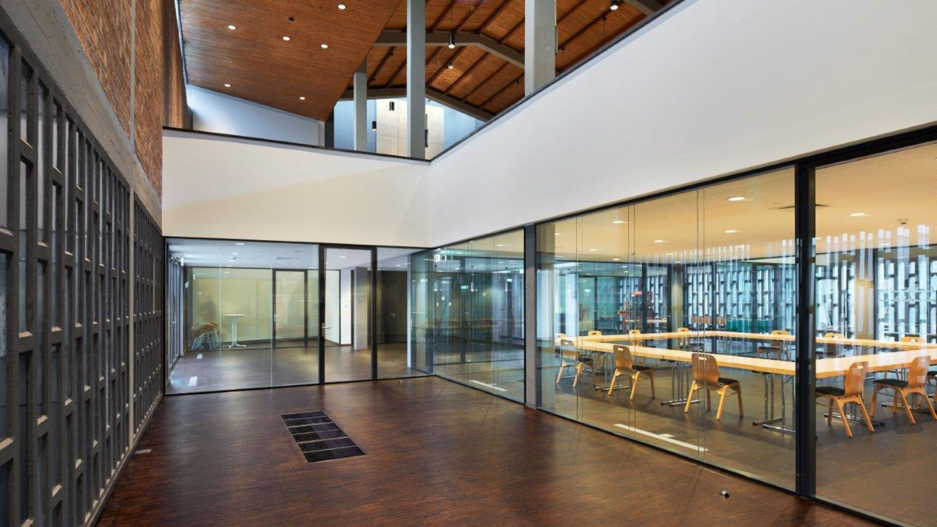 Innenansicht des neuen Gemeindesaals der Kirche Rüsselsheim mit Glaswänden, Sichtbeton und Holzdecke.