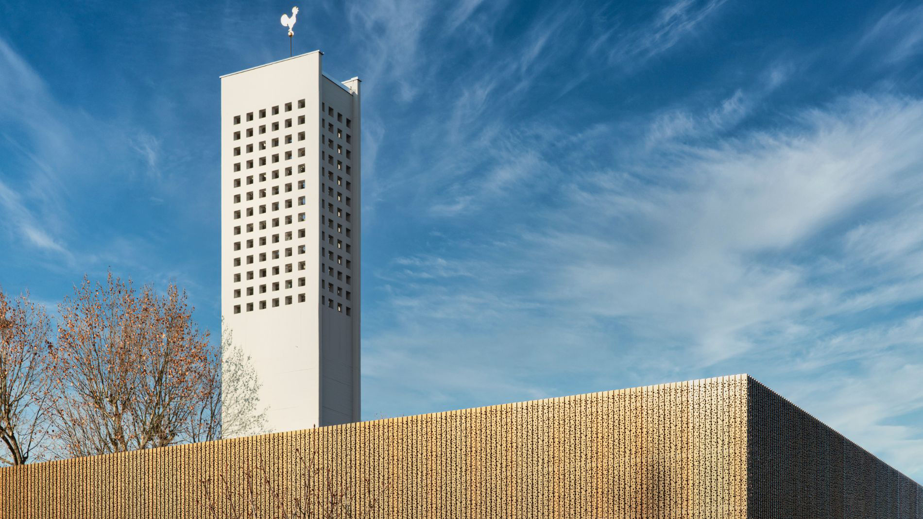 Fassadendetail der sanierten Kirche Haßloch Nord mit hellem Glockenturm und moderner Holzverkleidung.
